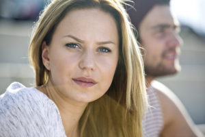 Pretty young woman looking into the camera with her boyfriend out of focus in the background