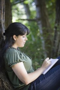 young woman writing in a journal outside