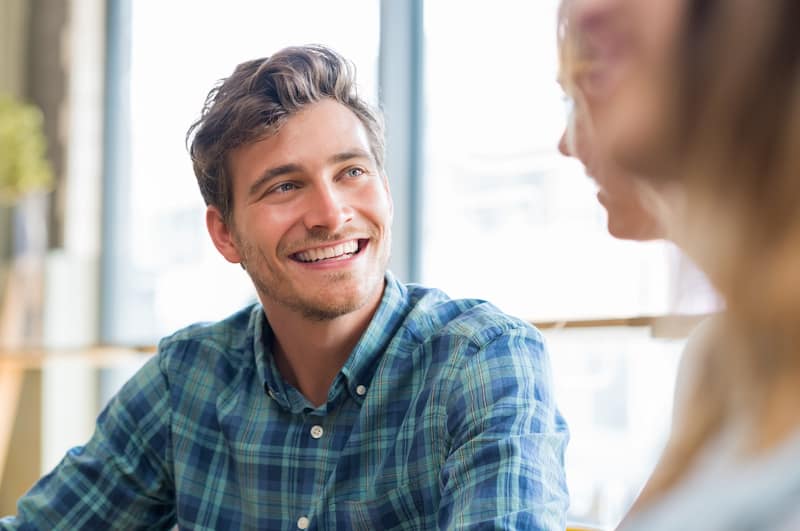 Closeup of cheerful young man in conversation with woman in cafeteria. Happy young couple talking an