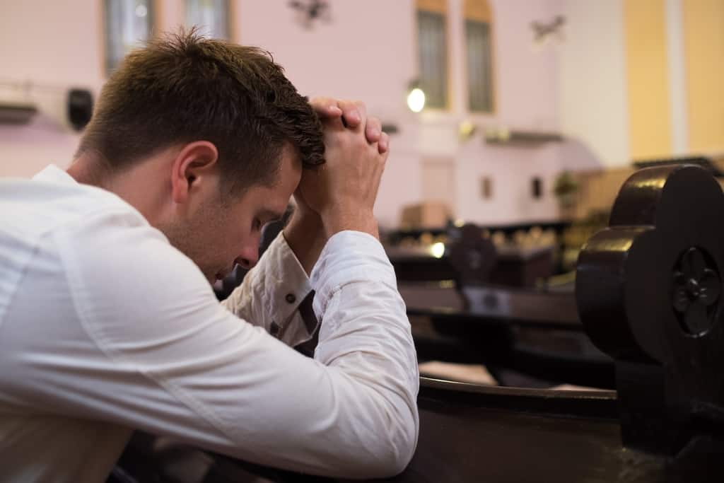 Man in a church, praying for the strength to overcome his addiction.