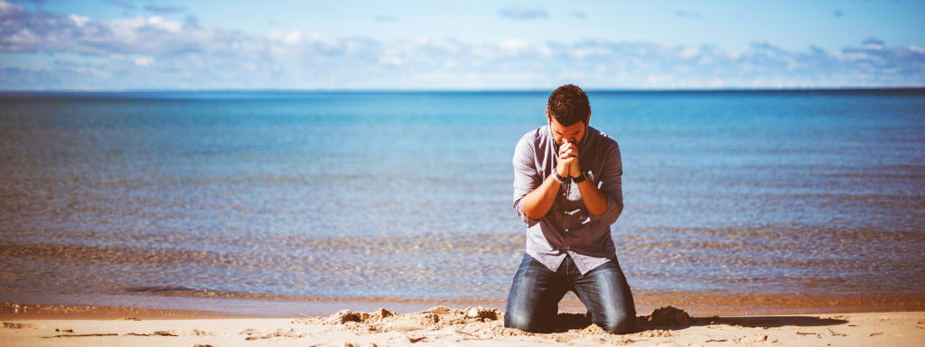 Man praying on beach looking for guidance to recover from addiction