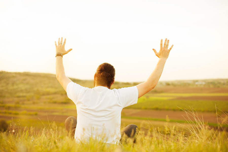 A man rejoices in a field by holding his arms up in the air.