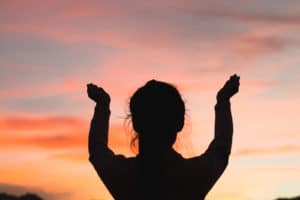 A silhouette of a woman with her hands raised to the sky.