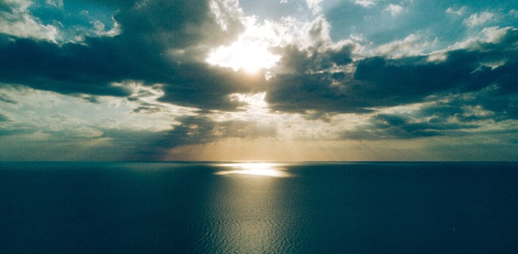 A tranquil ocean horizon, where the sun's rays pierce through clouds, capturing the essence of the serenity prayer and the peaceful journey of addiction recovery.