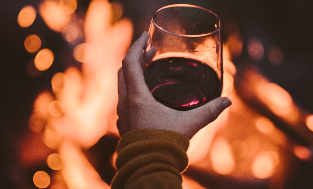 A glass of wine illuminated by the warm glow of a bonfire, representing the allure of alcohol and the dangers lurking beneath its charm.