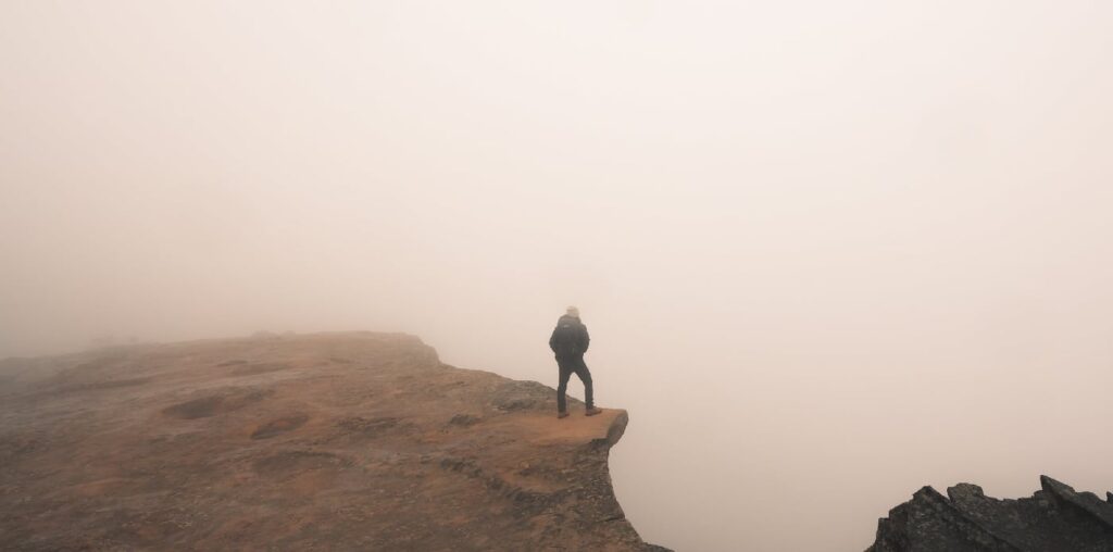 2. Man standing precariously at the edge of a fog-covered cliff, symbolizing the unknown and potentially dangerous effects of stimulants on the mind and body.
