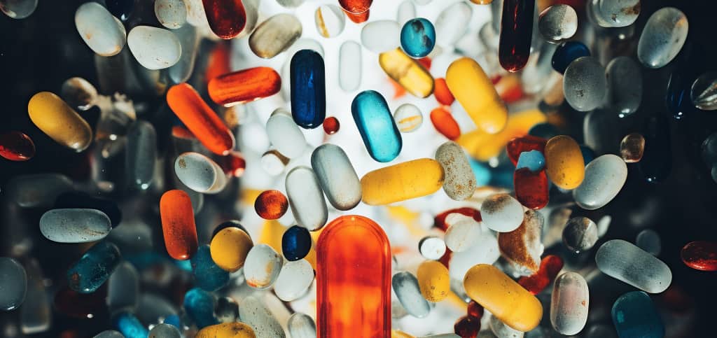 A diverse array of colorful pills in various shapes and sizes scattered chaotically, representing the complexity and dangers discussed in 'What is the Blue Pill?'