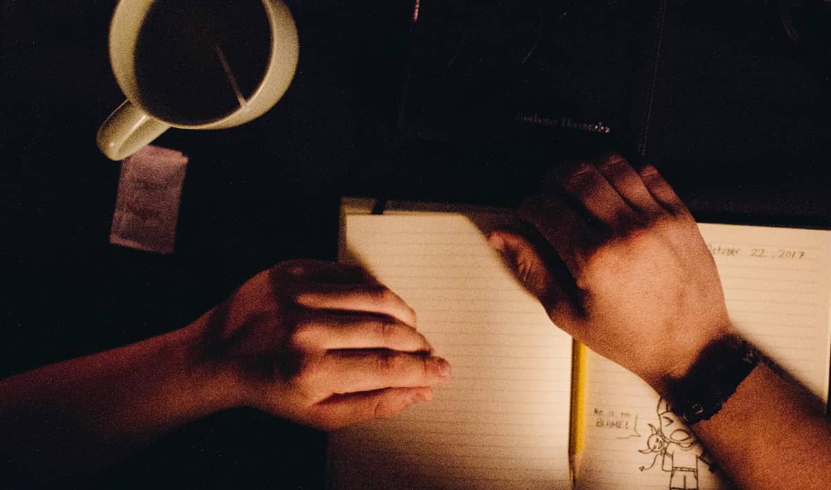 Close up of man hands journaling with a cup of tea to show his daily reprieve in addiction recovery