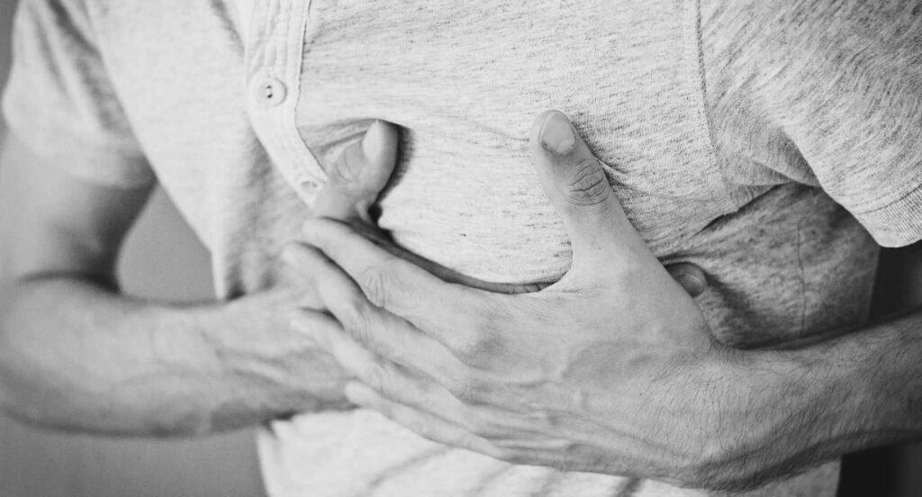 Black and white image of man holding his heart wondering, Why Do I Get Chest Pain After Drinking Alcohol?