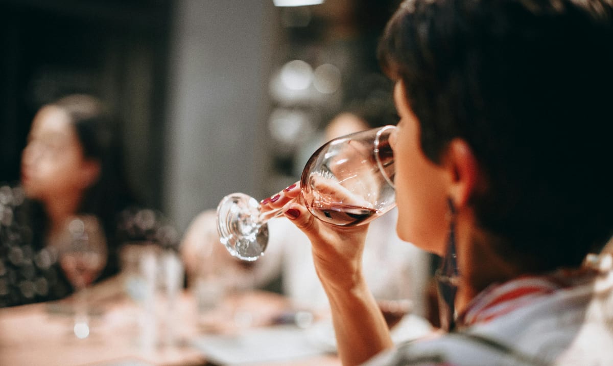 Image of a woman finishing a glass of wine at a dinner party showing that heavy drinking can come in many forms and is bad for your heart