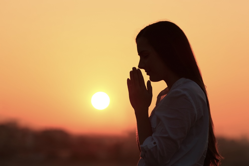 Silhouette of a female praying with sunset behind her