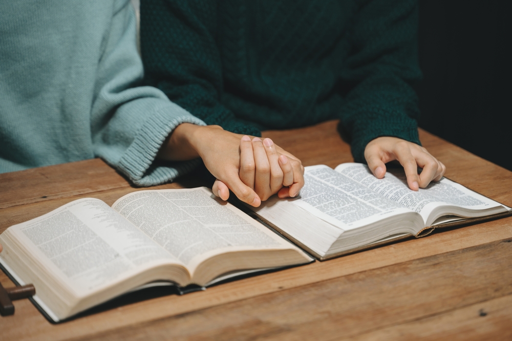 Two people hold hands while reading the Bible.