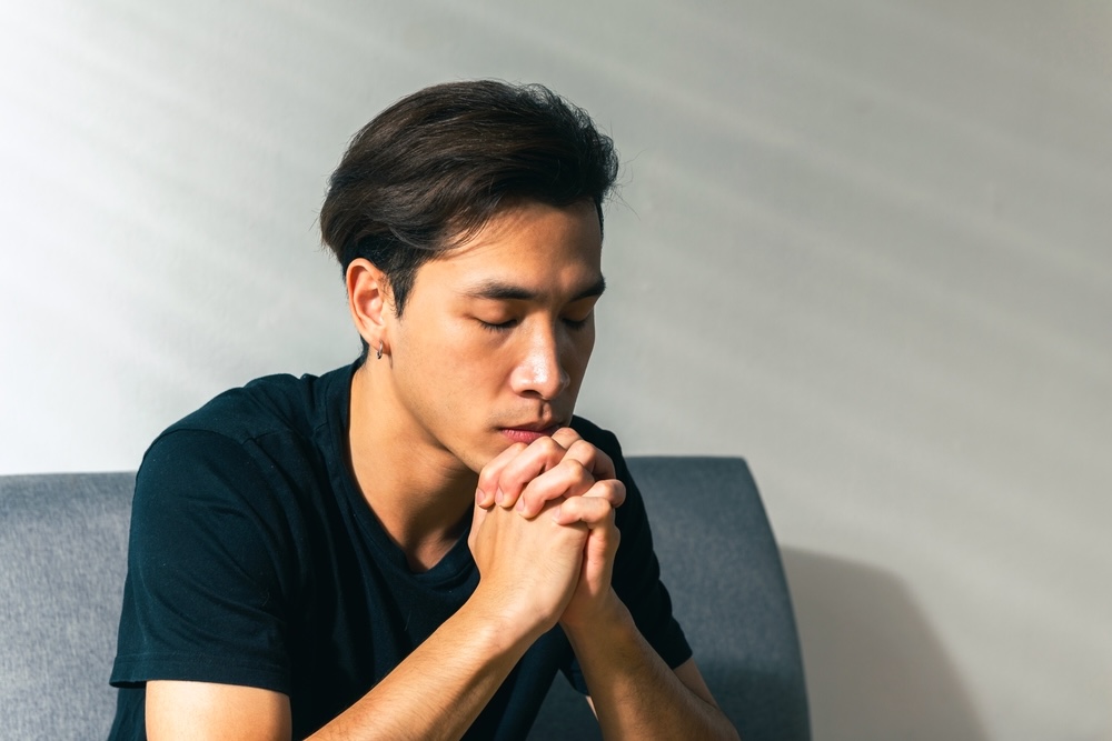 Man wearing a black shirt with closed eyes praying while in Christian alcohol rehab