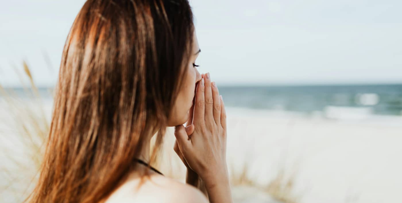 Woman prays while sitting at the beach showing peace and calm and effective christian rehab.