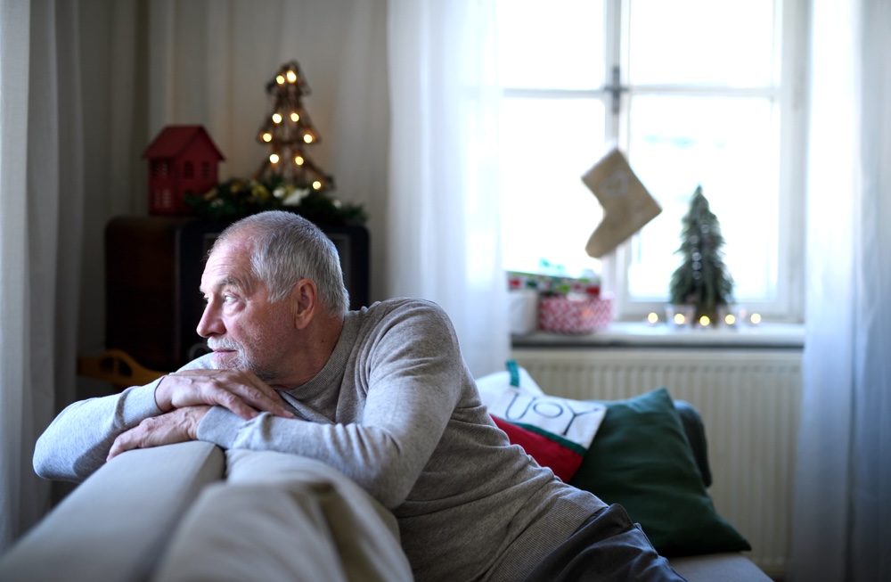 Senior man looking out of the window feeling lonely during the holiday season 