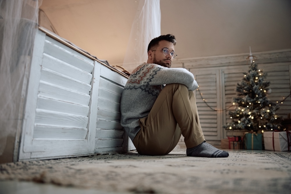 Depressed man sitting on the floor with a Christmas tree